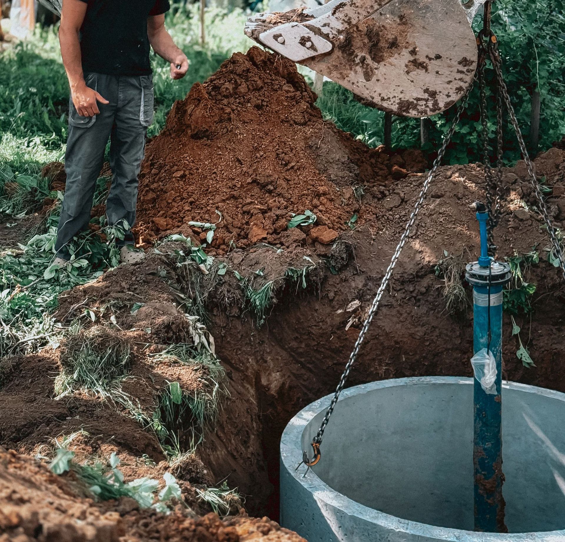 A construction worker supervises the installation of a concrete well using heavy machinery in a backyard project.
