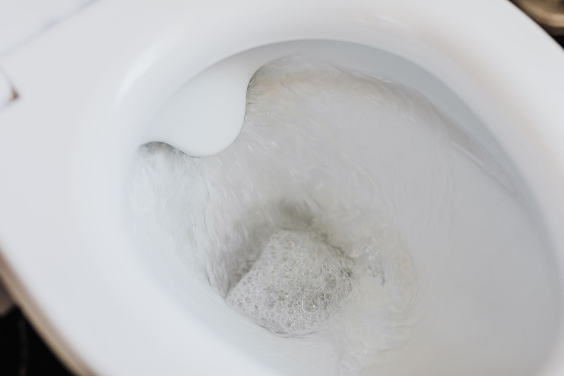 High angle of clean white ceramic toilet bowl with flushing foamy water in bathroom
